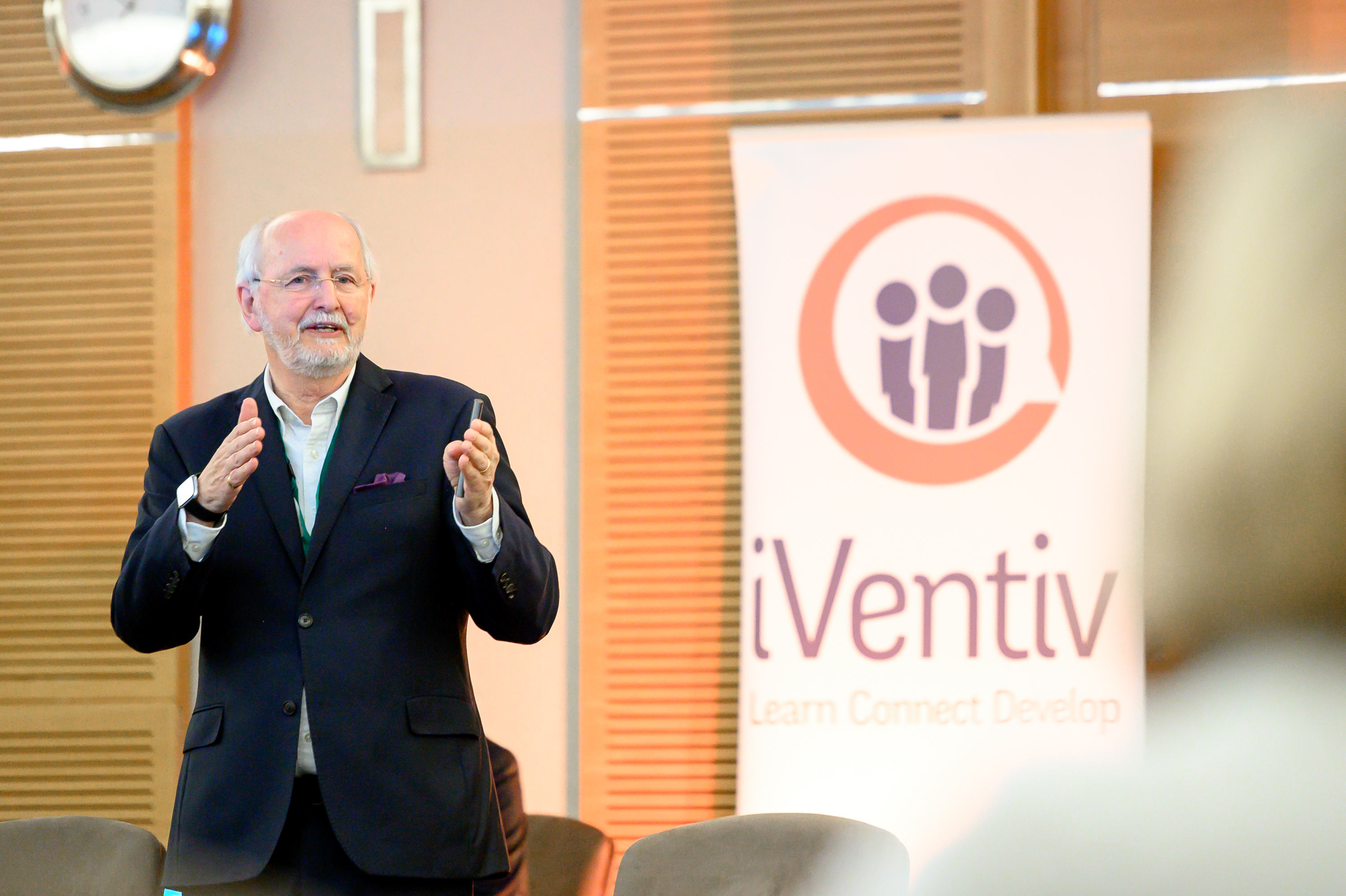 A man, Charles Jennings, in business dress, stands and speaks in front of an iVentiv banner.