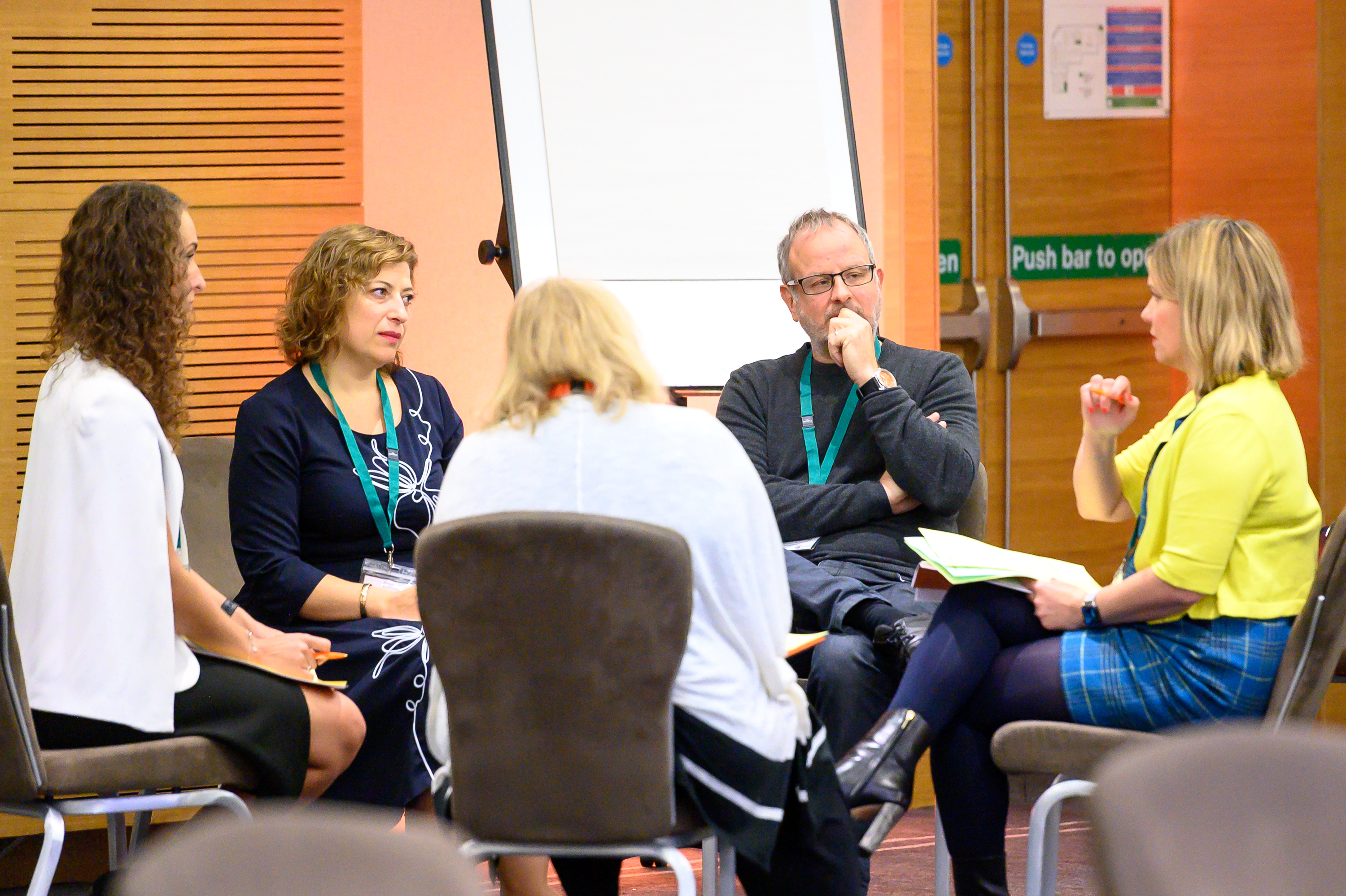 Five people sit in a small circle at an executive conference in conversation.